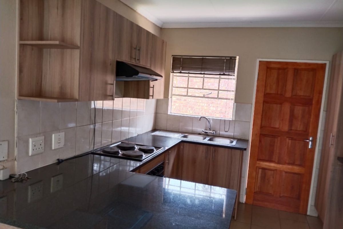 A functional kitchen featuring laminate cabinetry, granite countertops, an electric hob with extractor fan, and a double sink with tiled backsplash.