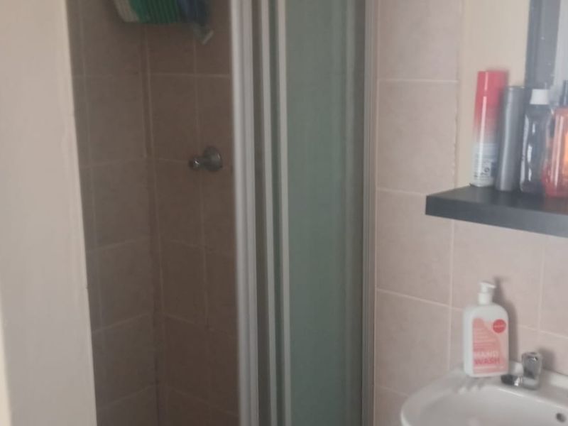A functional bathroom featuring a shower enclosure with tiled walls, a pedestal basin with mixer tap, and a wall-mounted floating shelf.