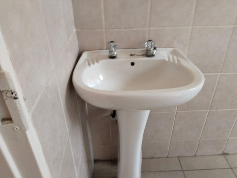 A compact bathroom featuring a white pedestal basin with chrome taps, complemented by neutral ceramic wall and floor tiling.