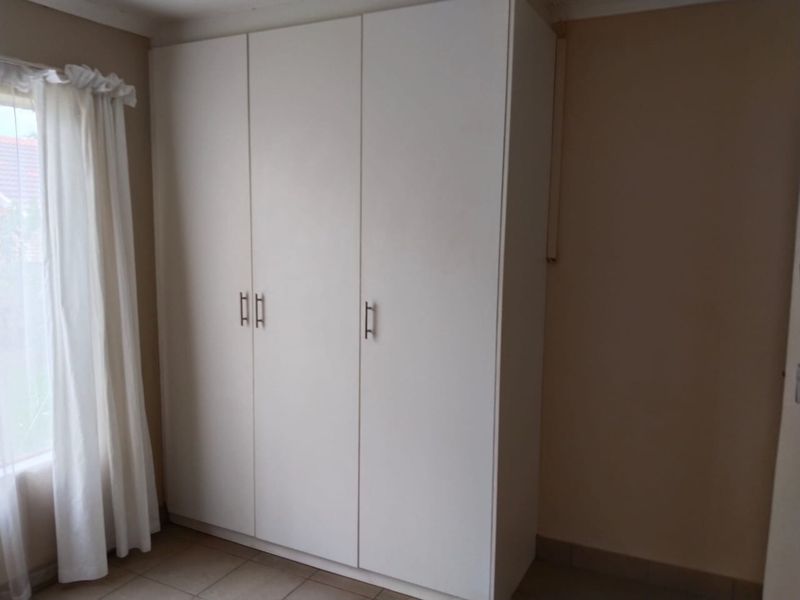 A bedroom featuring a clean, white built-in wardrobe and neutral tiled flooring, offering a bright and functional storage space.