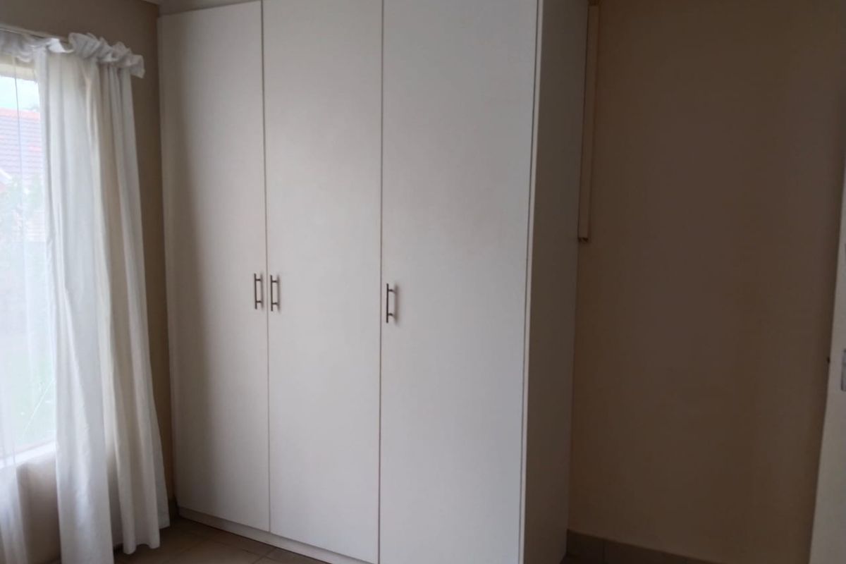 A bedroom featuring a clean, white built-in wardrobe and neutral tiled flooring, offering a bright and functional storage space.