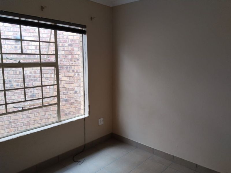 An empty bedroom featuring tiled flooring and a window with security bars, requiring minor cosmetic repairs to the window frame and wall fixtures.