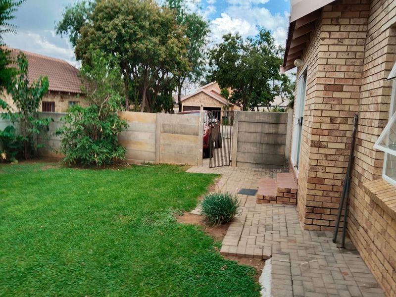 A private rear garden featuring a paved patio area, a well-maintained lawn, and secure perimeter walling with a metal access gate.
