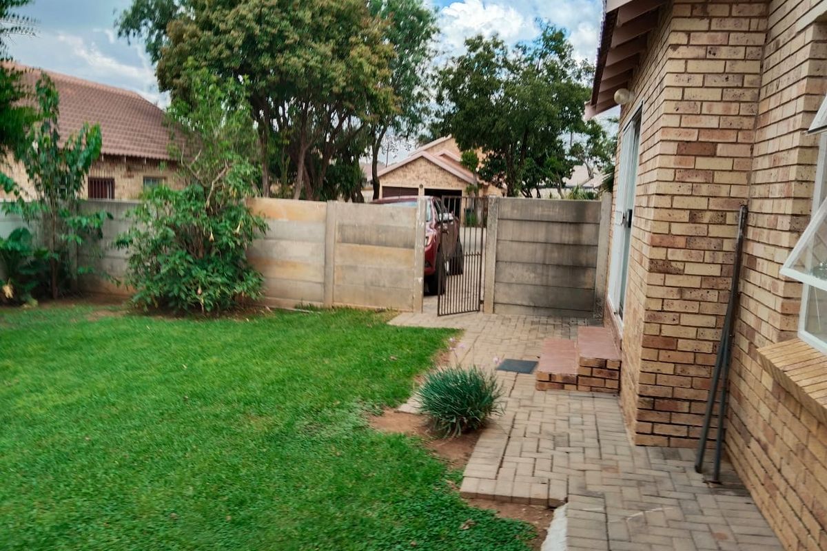 A private rear garden featuring a paved patio area, a well-maintained lawn, and secure perimeter walling with a metal access gate.