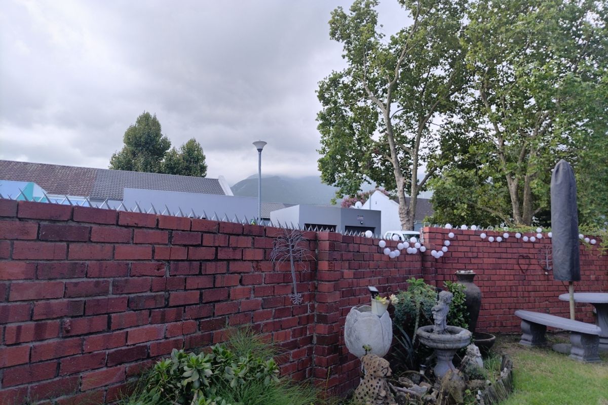 A private rear garden featuring a solid red brick boundary wall topped with security spikes, overlooking neighbouring properties and distant mountain views.