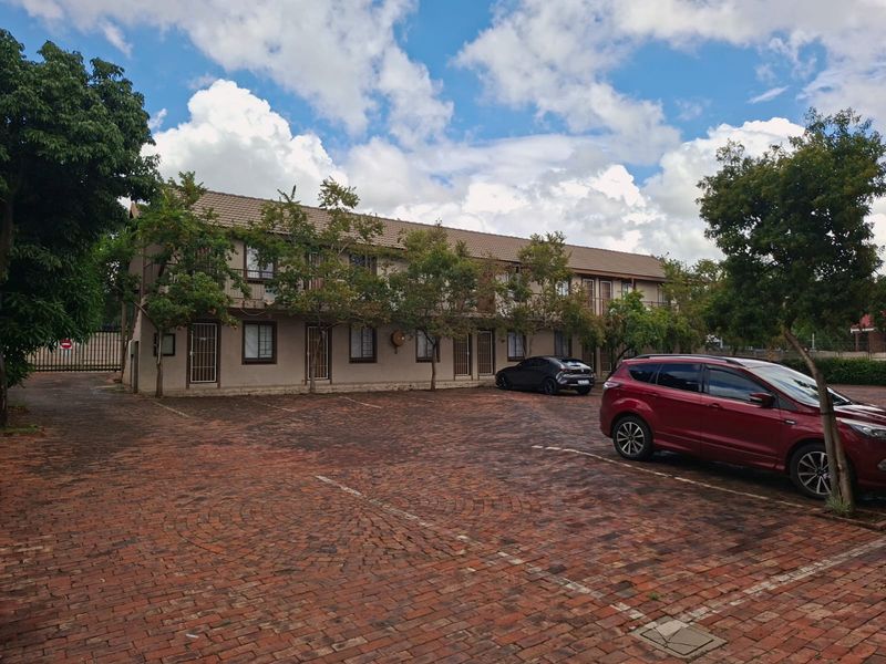 Exterior view of a multi-story apartment complex featuring a brick-paved parking area and established trees in front of the building facade.