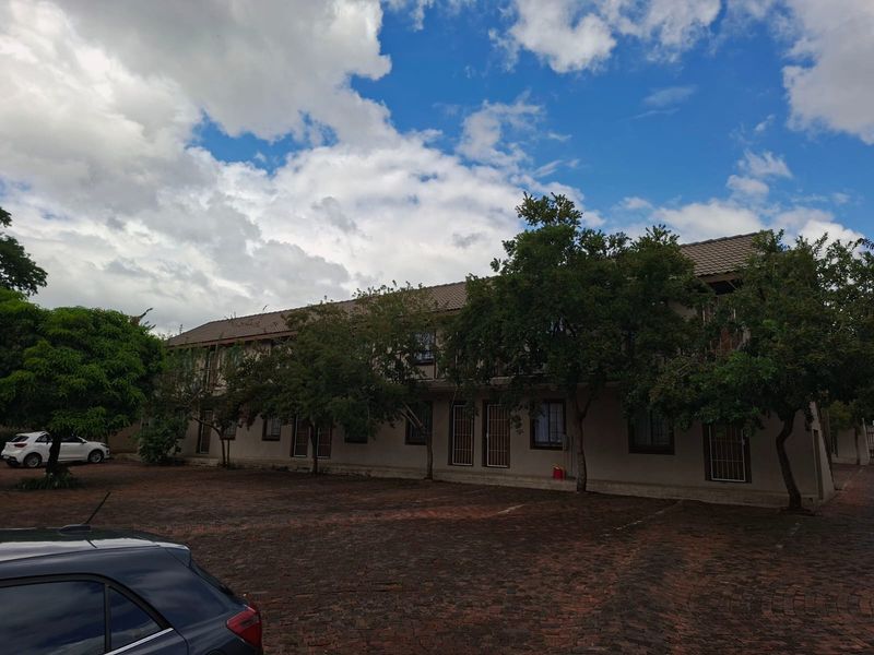 Exterior view of a multi-story apartment complex featuring a paved driveway, tiled roof, and security-fitted windows and doors.