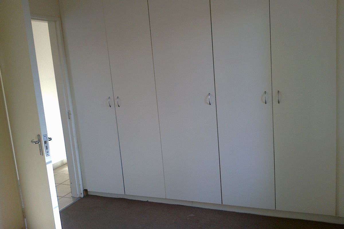 A bedroom featuring a wall of built-in cupboards and carpeted flooring, presented in an empty state.