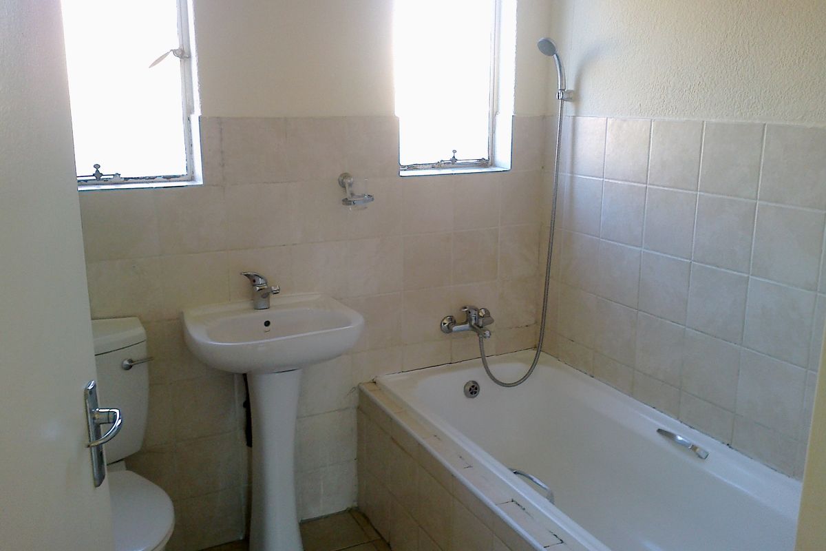 A functional bathroom featuring a pedestal basin, toilet, and a bathtub with a shower mixer, finished with neutral wall tiling.