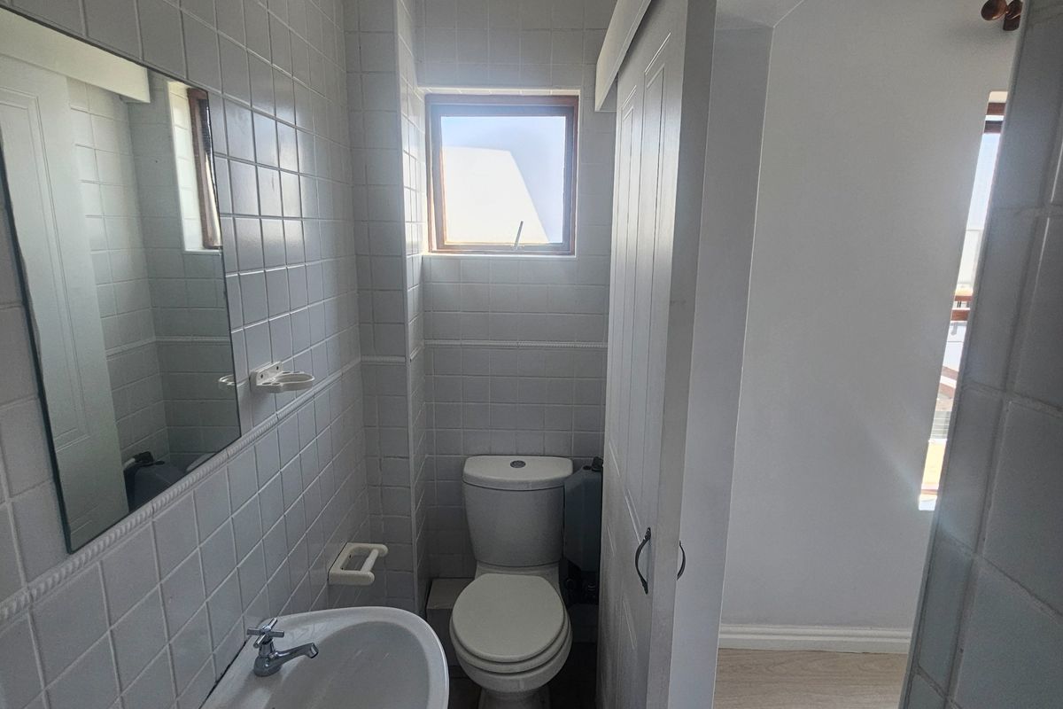 A compact bathroom featuring a pedestal basin, toilet, and tiled walls, accessible via a sliding door.