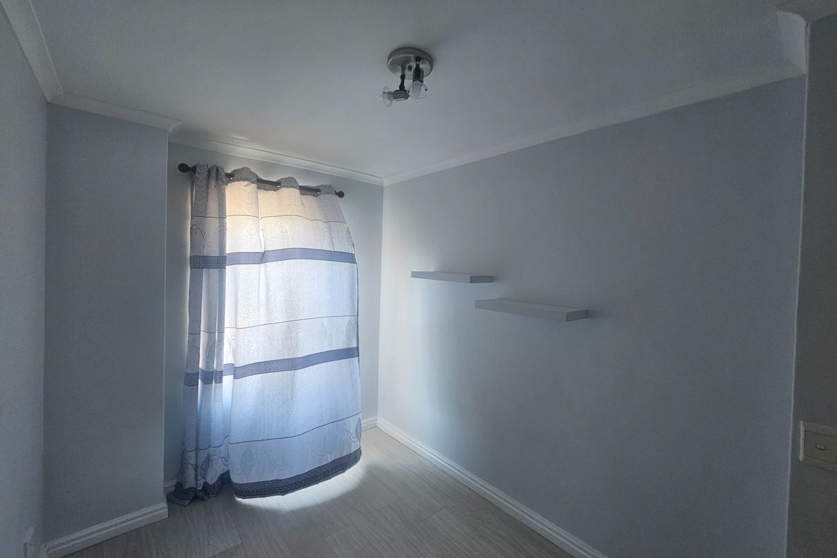 A bright, empty bedroom featuring light-toned wood-look flooring, neutral walls, crown molding, and two built-in floating shelves.