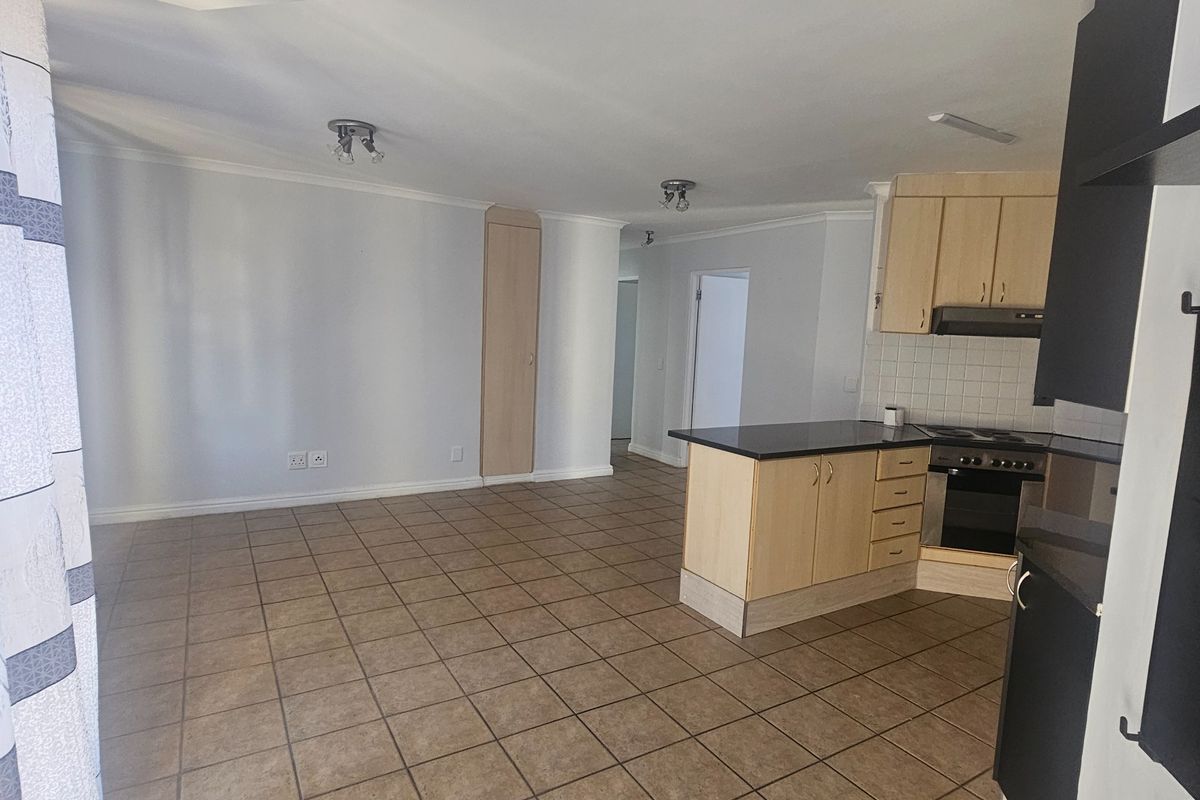 Open plan living area featuring tiled flooring and a functional kitchen with built-in cabinetry, oven, and hob.