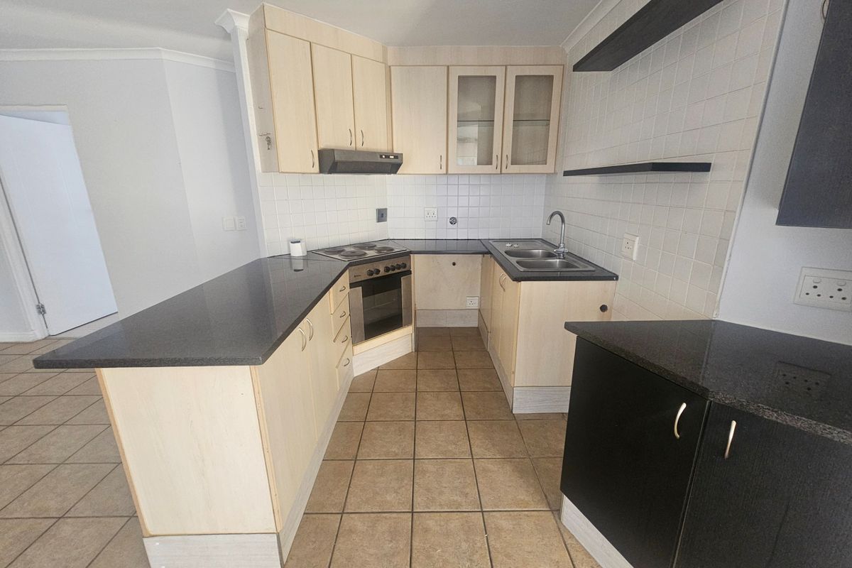 A functional kitchen featuring light wood cabinetry, dark countertops, a built-in oven with hob, and tiled flooring.