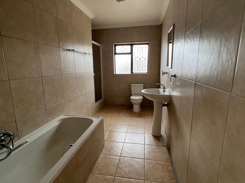A spacious, fully tiled bathroom featuring a bathtub, pedestal sink, toilet, and a separate shower enclosure.
