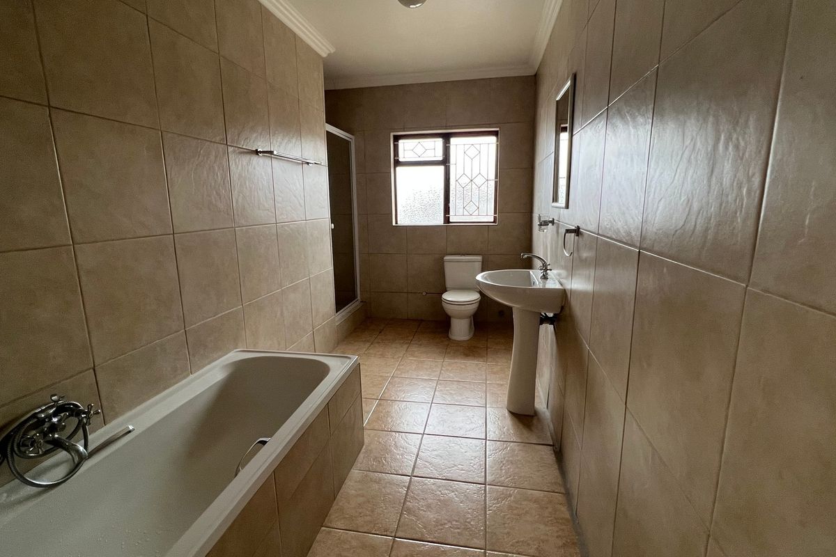 A spacious, fully tiled bathroom featuring a bathtub, pedestal sink, toilet, and a separate shower enclosure.