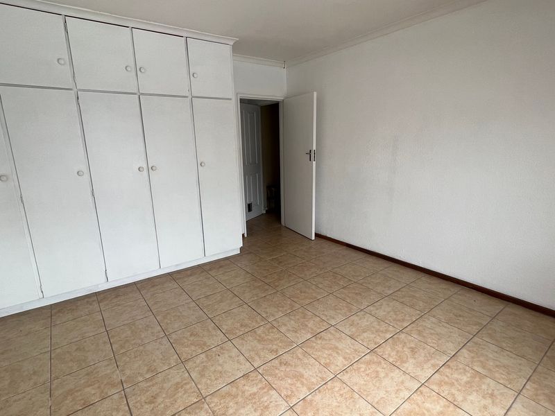 An empty bedroom featuring tiled flooring and extensive white built-in cupboards, providing ample storage space.