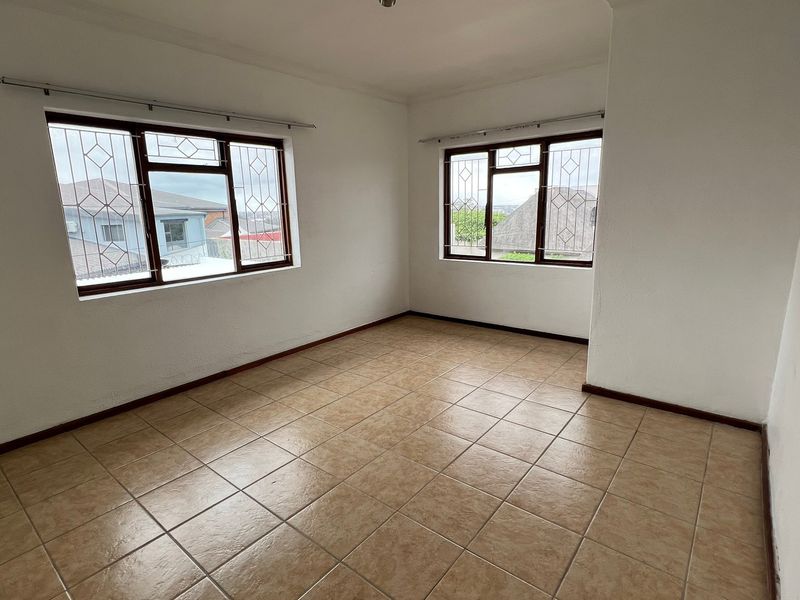 A bright, empty bedroom featuring neutral tiled flooring, white walls, and windows fitted with security bars and curtain rails.