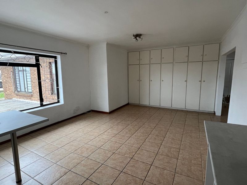 Spacious open-plan living area featuring neutral tiled flooring, extensive built-in storage cupboards, and large windows with security bars.