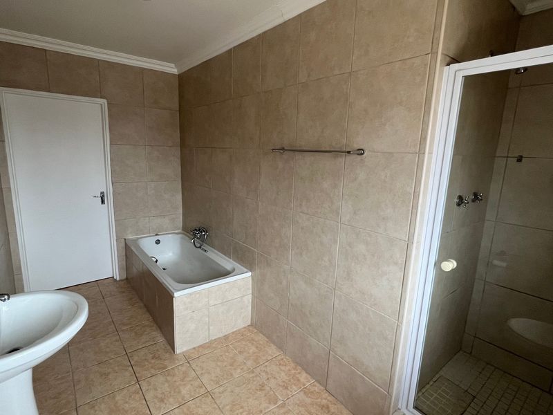 A spacious bathroom featuring a pedestal basin, a built-in bathtub, and a separate shower enclosure with neutral wall and floor tiling.