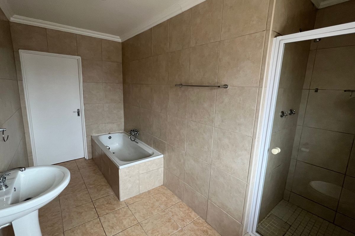A spacious bathroom featuring a pedestal basin, a built-in bathtub, and a separate shower enclosure with neutral wall and floor tiling.