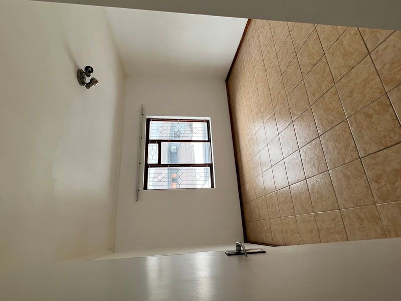 An empty bedroom featuring neutral tiled flooring, a window with security bars, and a wall-mounted light fixture.
