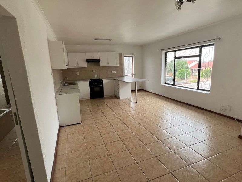 Open-plan kitchen and living area featuring tiled flooring, built-in cabinetry, a breakfast counter, and large windows with security bars.