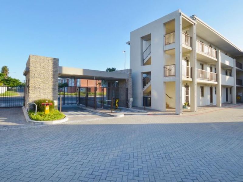 Exterior view of the apartment complex entrance featuring a secure gated access point, paved driveway, and multi-story building with balconies.
