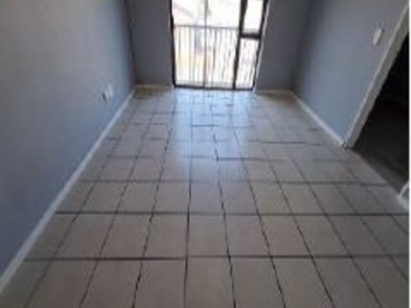 An empty living room featuring tiled flooring and a sliding glass door leading to a balcony.