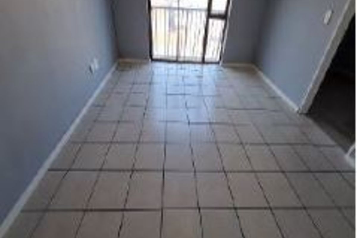 An empty living room featuring tiled flooring and a sliding glass door leading to a balcony.