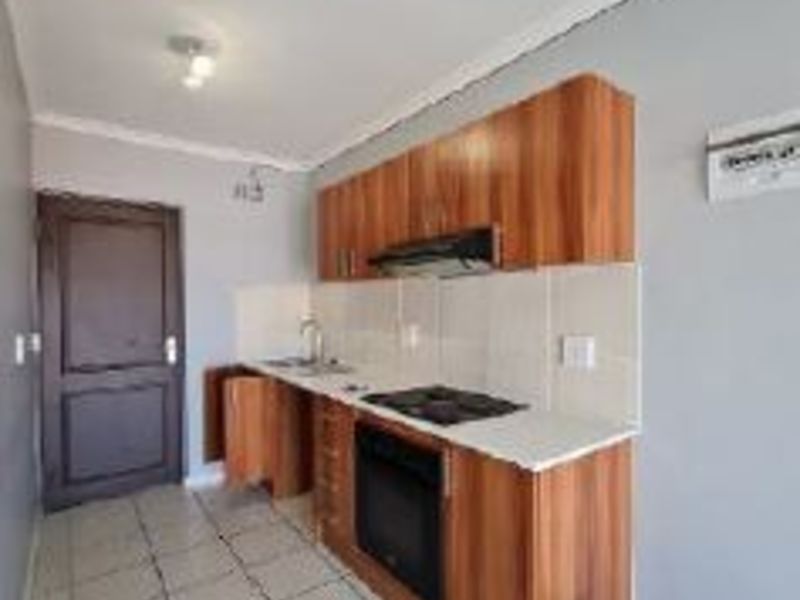 A compact kitchen featuring wood-finish cabinetry, built-in oven and hob, tiled splashbacks, and tiled flooring.