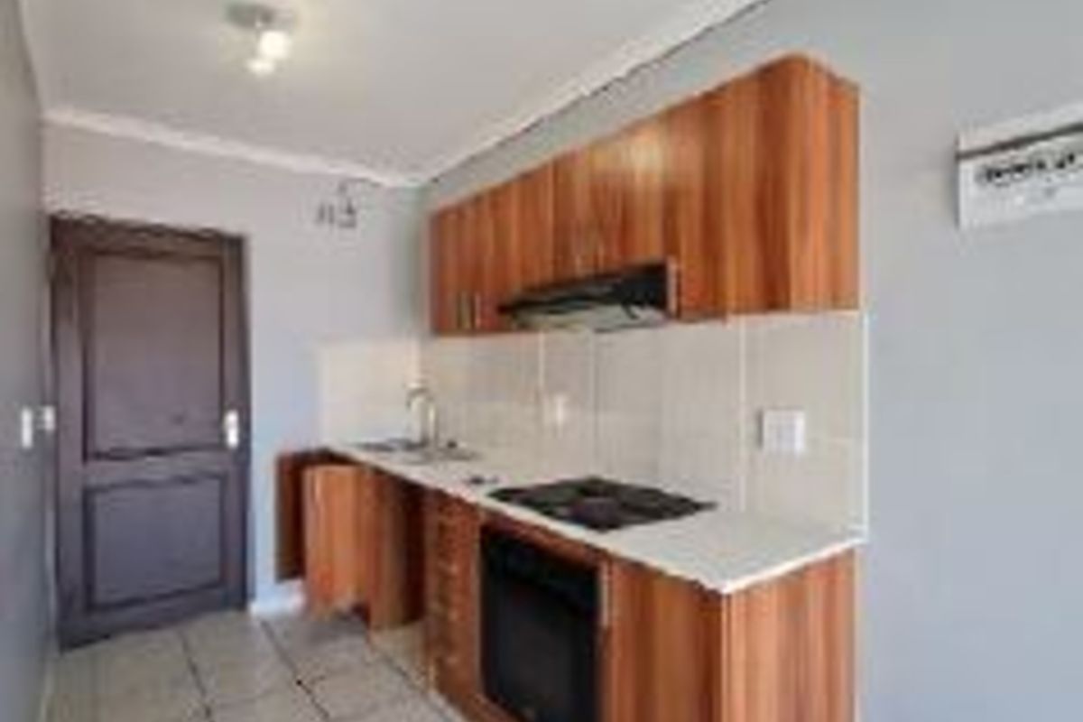 A compact kitchen featuring wood-finish cabinetry, built-in oven and hob, tiled splashbacks, and tiled flooring.