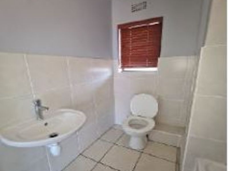 A functional bathroom featuring tiled walls and flooring, a wall-mounted basin, and a standard toilet with a window blind.