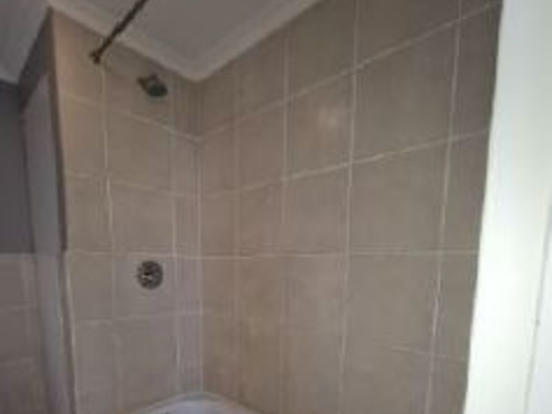 A functional bathroom featuring a built-in bathtub with a shower head and neutral wall tiling.
