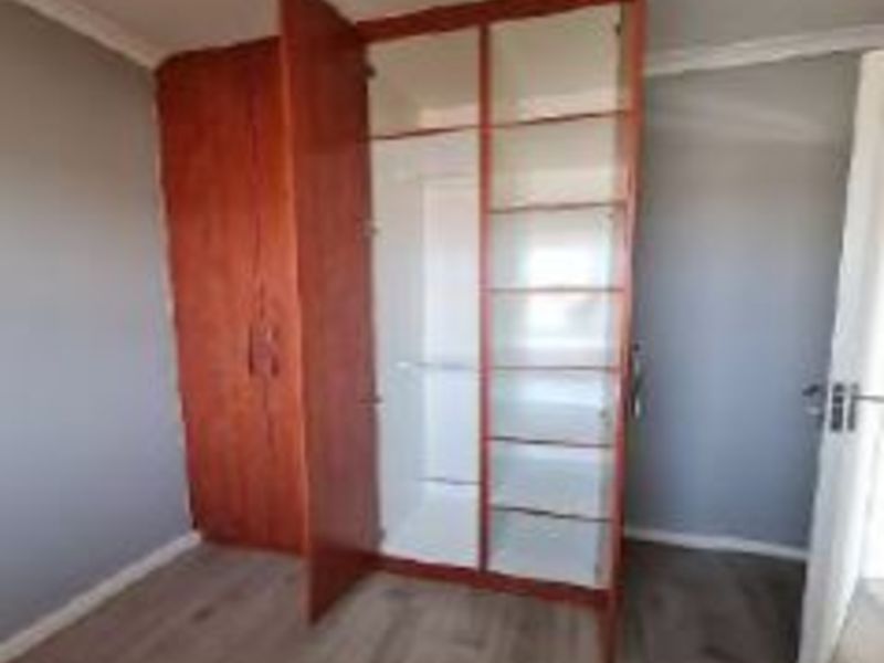 A clean, empty bedroom featuring light-toned laminate flooring and a large, functional built-in wooden wardrobe with shelving and hanging space.