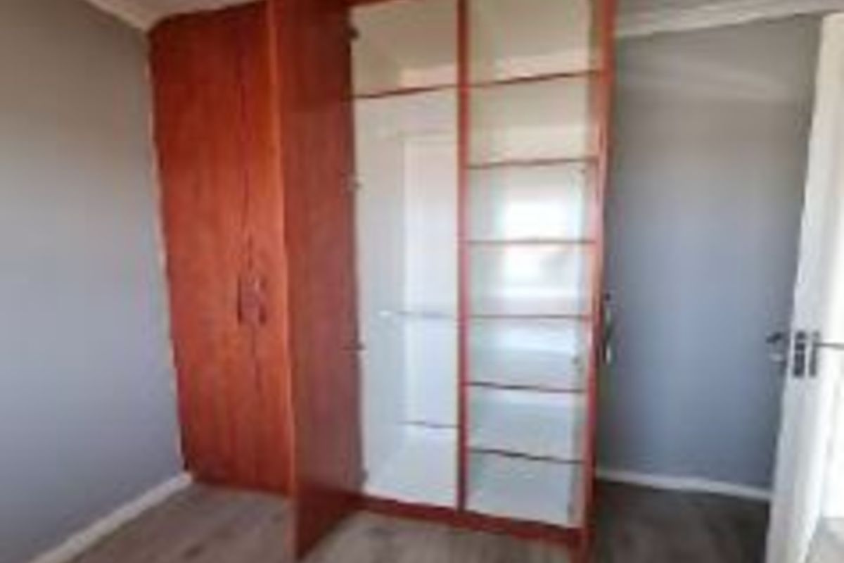 A clean, empty bedroom featuring light-toned laminate flooring and a large, functional built-in wooden wardrobe with shelving and hanging space.
