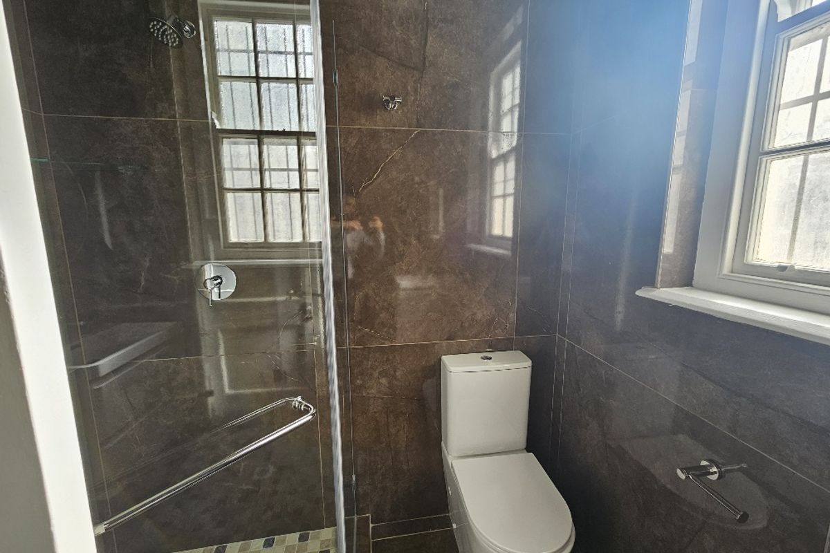 A modern bathroom featuring dark marble-style wall tiles, a glass-enclosed shower, and a white ceramic toilet.