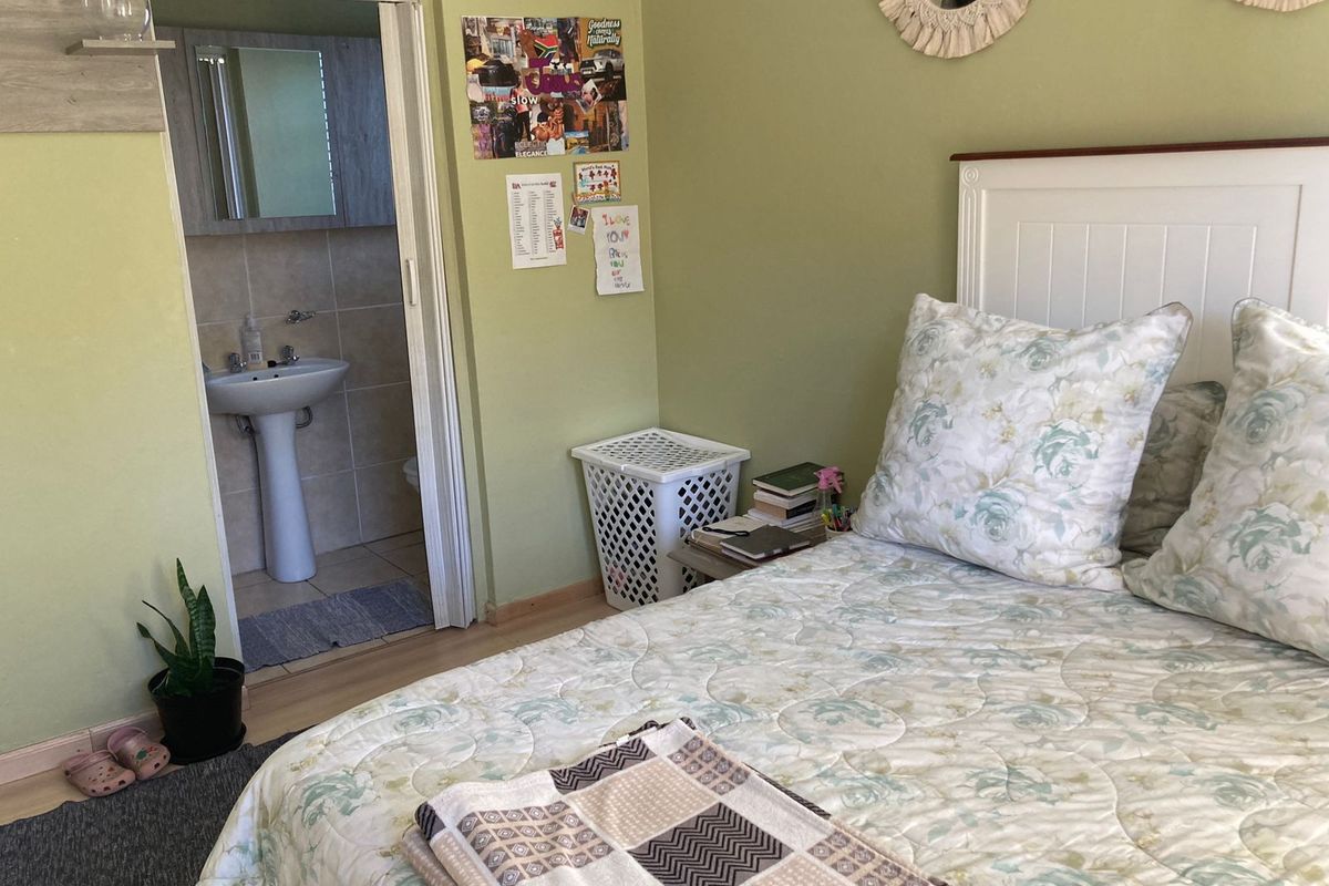 A bedroom featuring light green walls and laminate flooring, with an adjoining en-suite bathroom equipped with a pedestal sink.