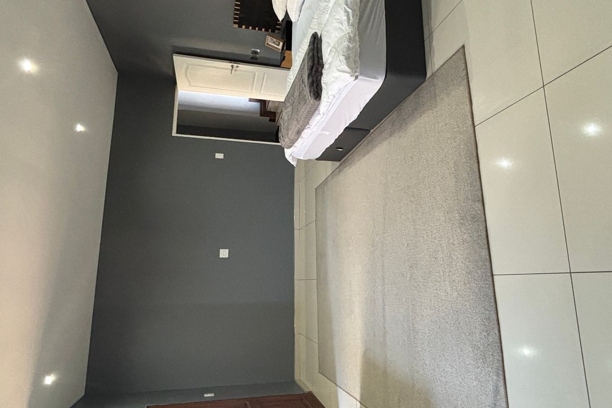 A bedroom featuring dark grey accent walls, large format floor tiles, and recessed downlighting.