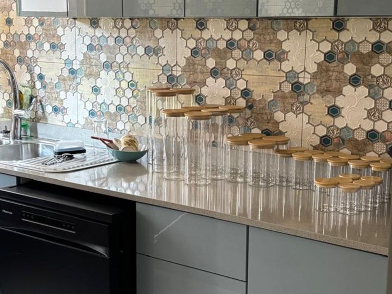 A modern kitchen area featuring a stone countertop, stainless steel sink with gooseneck faucet, integrated dishwasher, and a decorative hexagonal mosaic tile backsplash.