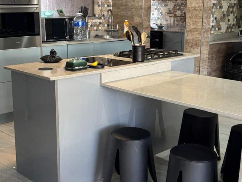 Modern kitchen featuring a central island with a built-in gas hob, stone countertops, and contemporary cabinetry with a decorative tiled backsplash.