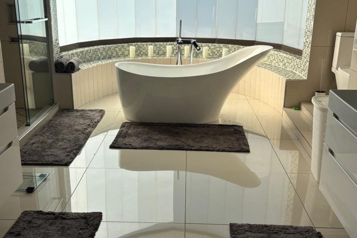 Modern bathroom featuring a sleek freestanding bathtub, mosaic tile accents, large windows, and high-gloss floor tiles for a bright, contemporary aesthetic.