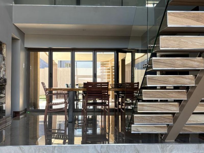 Modern living area featuring a striking floating staircase with glass balustrade, high-gloss tiled flooring, and large bi-fold doors opening to the exterior.
