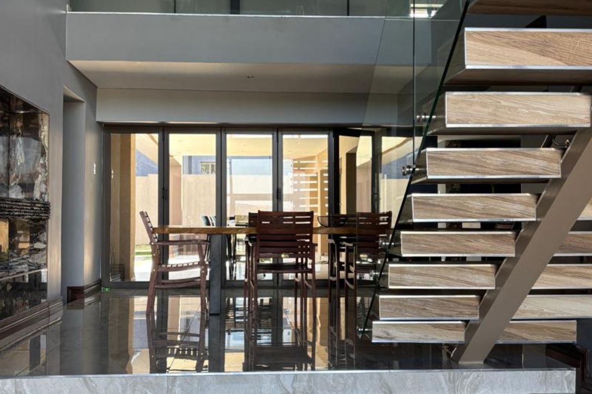 Modern living area featuring a striking floating staircase with glass balustrade, high-gloss tiled flooring, and large bi-fold doors opening to the exterior.