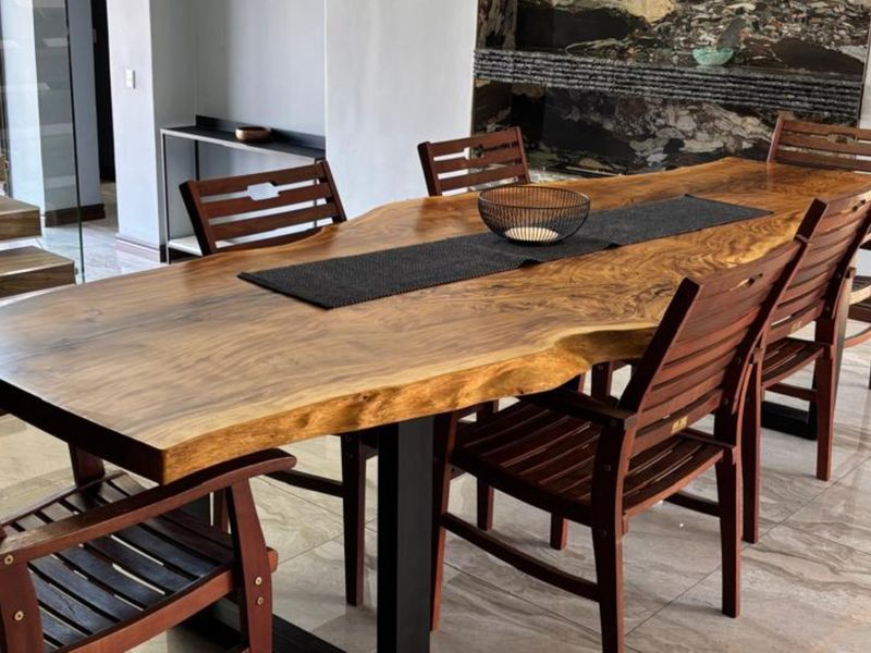 Modern dining area featuring a live-edge wooden table, polished tile flooring, and a striking stone feature wall with an adjacent floating staircase.