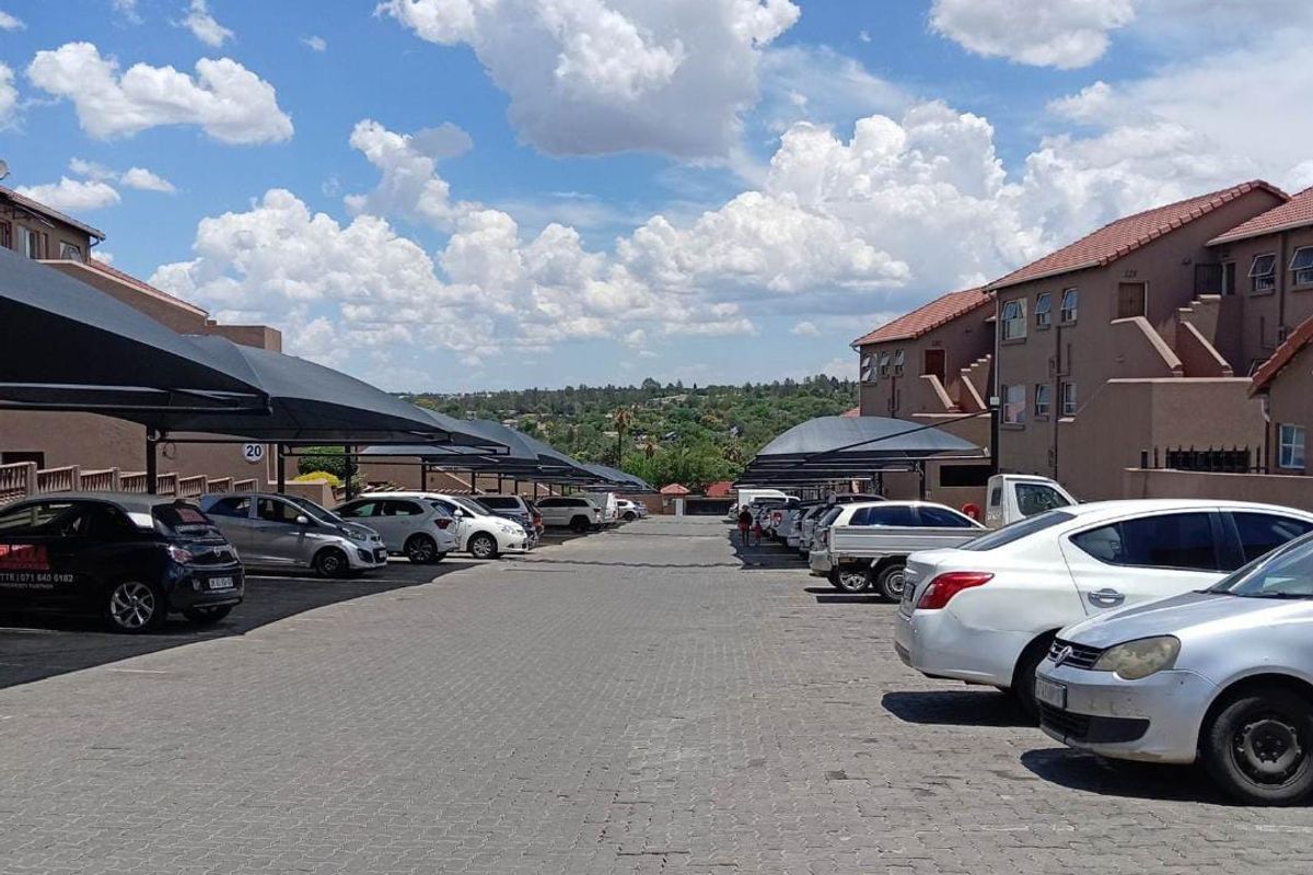Outdoor parking area featuring paved ground and covered shade-net parking bays for residents within the apartment complex.