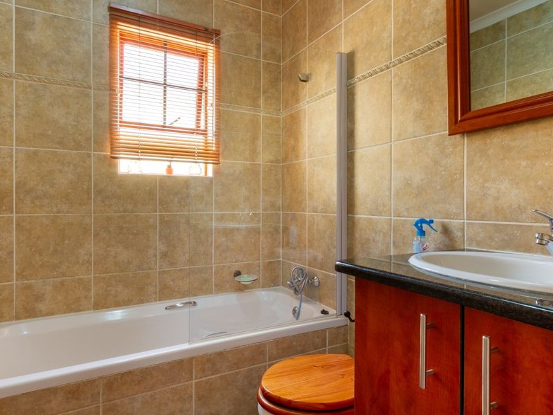 A functional bathroom featuring a built-in bathtub with a glass screen, a vanity cabinet with a granite countertop, and neutral wall tiling.