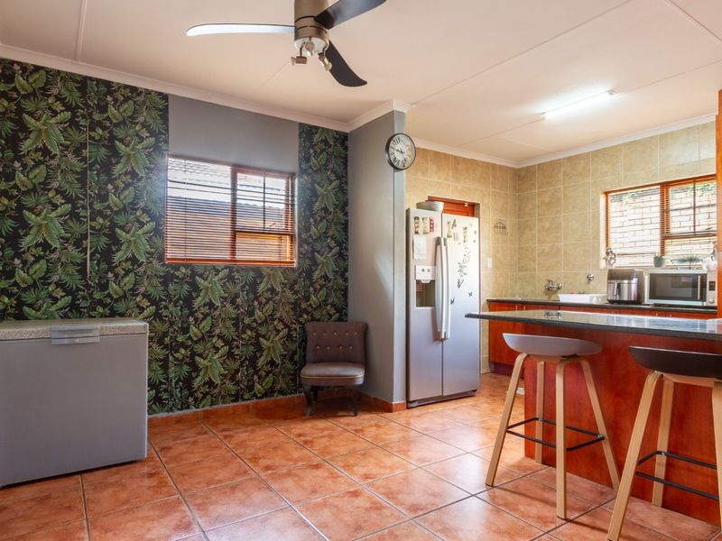 Open-plan kitchen and dining area featuring tiled flooring, wooden cabinetry, granite countertops, a breakfast bar, and a ceiling fan.