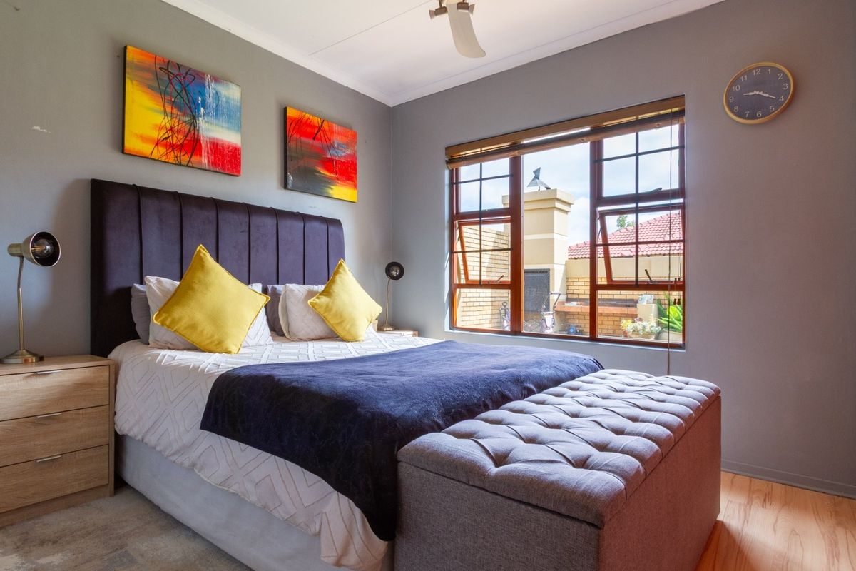 A well-maintained bedroom featuring grey walls, a built-in wardrobe, a ceiling fan, and a window with wooden blinds overlooking the exterior area.