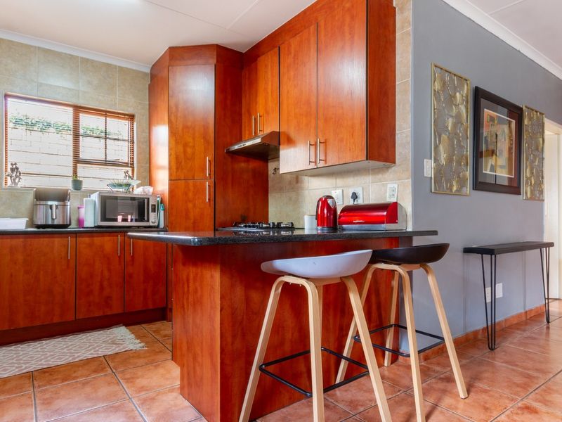 A functional kitchen featuring warm-toned wooden cabinetry, granite countertops, a breakfast bar, and tiled flooring with a practical layout.