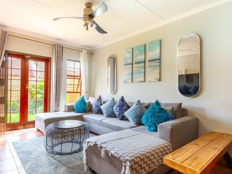 A bright living room featuring tiled flooring, a ceiling fan, and french doors providing access to the outdoor area.